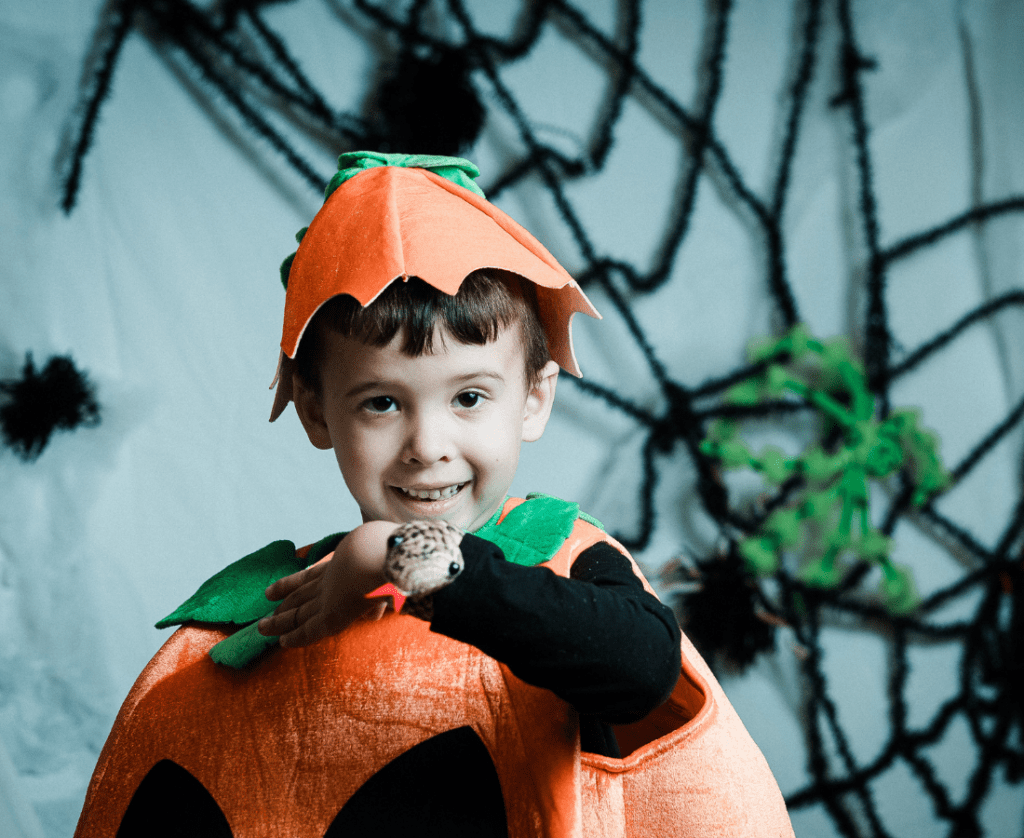 Little boy in pumpkin costume poses in front of spider web at Creepy Crawl Day with reptile poking out of his sleeve.